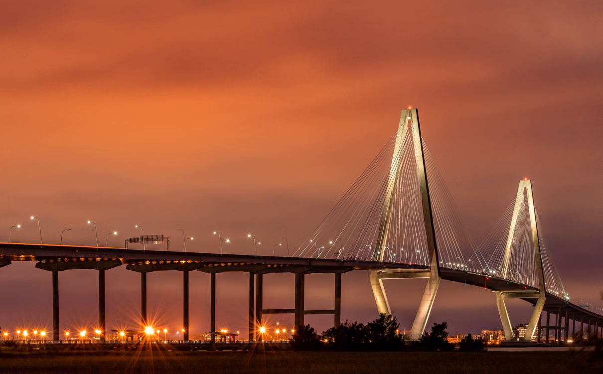 Photograph of the illuminated Arthur Ravenel Jr. Bridge in Charleston beneath a warm sunset sky